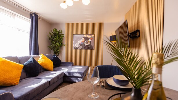 Un salon moderne avec un canapé gris, des coussins jaunes et noirs, un verre à vin en verre et une bouteille de vin posée sur une table ronde.