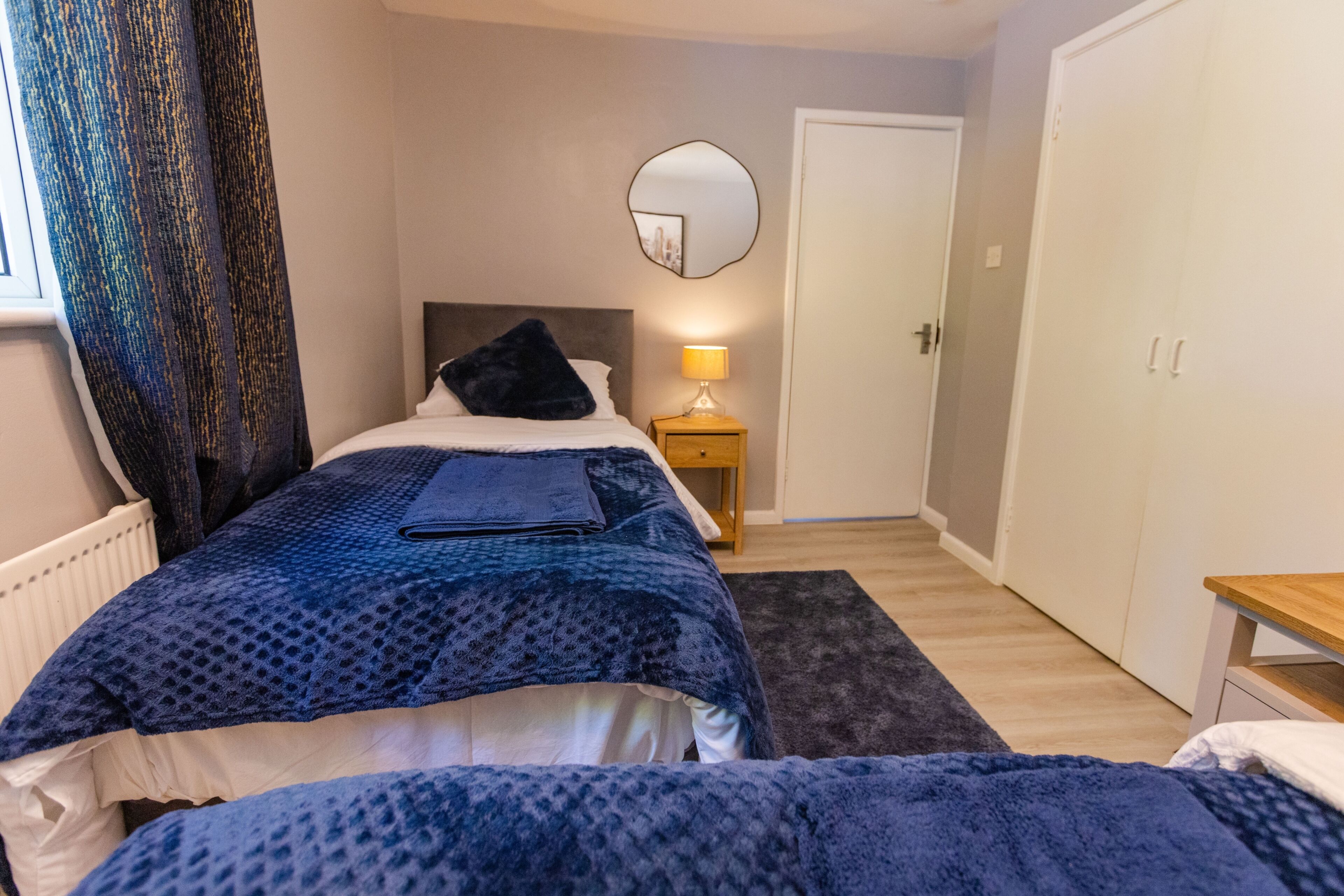 Een slaapkamer met een bed, nachtkastje, lamp en een kledingkast.