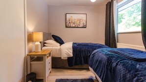 Une chambre à coucher avec un lit, une table de chevet, une lampe et un tableau représentant un paysage urbain accroché au mur.