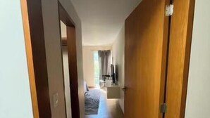 Ein Flur mit einer Holztür rechts, der zu einem Zimmer mit Bett und Fenster führt.