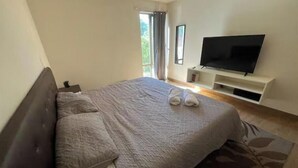 Ein Schlafzimmer mit einem Bett, einem Fernseher auf einem Schrank und einem Fenster mit Vorhängen.