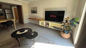 Ein modernes Wohnzimmer mit Flachbildfernseher, einem Essbereich mit Tisch und Stühlen sowie einer Zimmerpflanze.