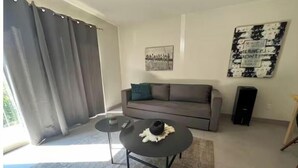 Ein modernes Wohnzimmer mit einem grauen Sofa, einem runden Couchtisch und einem großen Fenster mit grauen Vorhängen.