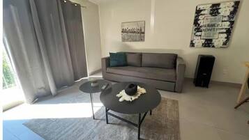 A modern living room with a grey sofa, a round coffee table, and a large window with grey curtains.