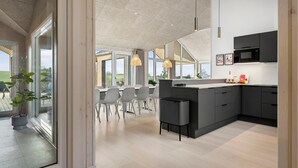 A modern kitchen with a large island, dark cabinetry, and a view of the outdoors through large windows.