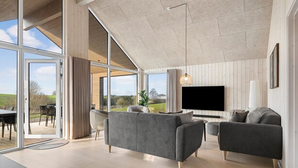 A modern living room with a large TV, grey sofas, and a view of the outdoors.