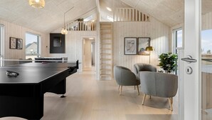 A spacious room with a pool table, two grey armchairs, and a staircase leading to an upper level.