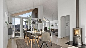 A modern kitchen with a large island, a dining area with a high ceiling, and a visible fireplace.