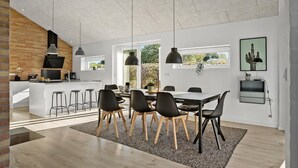 A modern kitchen with a brick wall, a dining area with a table and chairs, and a living space with a sofa and a TV.