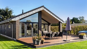A modern house with a glass extension, outdoor seating, and a garden.