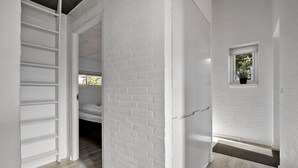A room with white brick walls, a wooden floor, a bunk bed, and a small window with a plant.