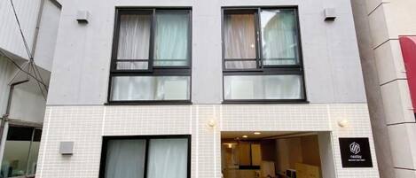 Un edificio de varios pisos con fachada de tejas, grandes ventanales y una entrada visible que conduce a una recepción.