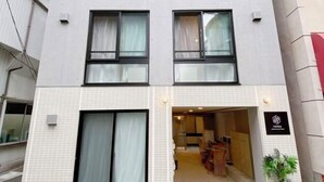 Ein mehrstöckiges Gebäude mit Kachelfassade, großen Fenstern mit Vorhängen und einem Eingang zu einer Rezeption.