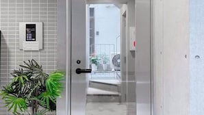 Ein moderner Aufzug mit Bedienfeld, einer Zimmerpflanze und Blick auf einen Balkon mit Geländer und einem Ventilator.