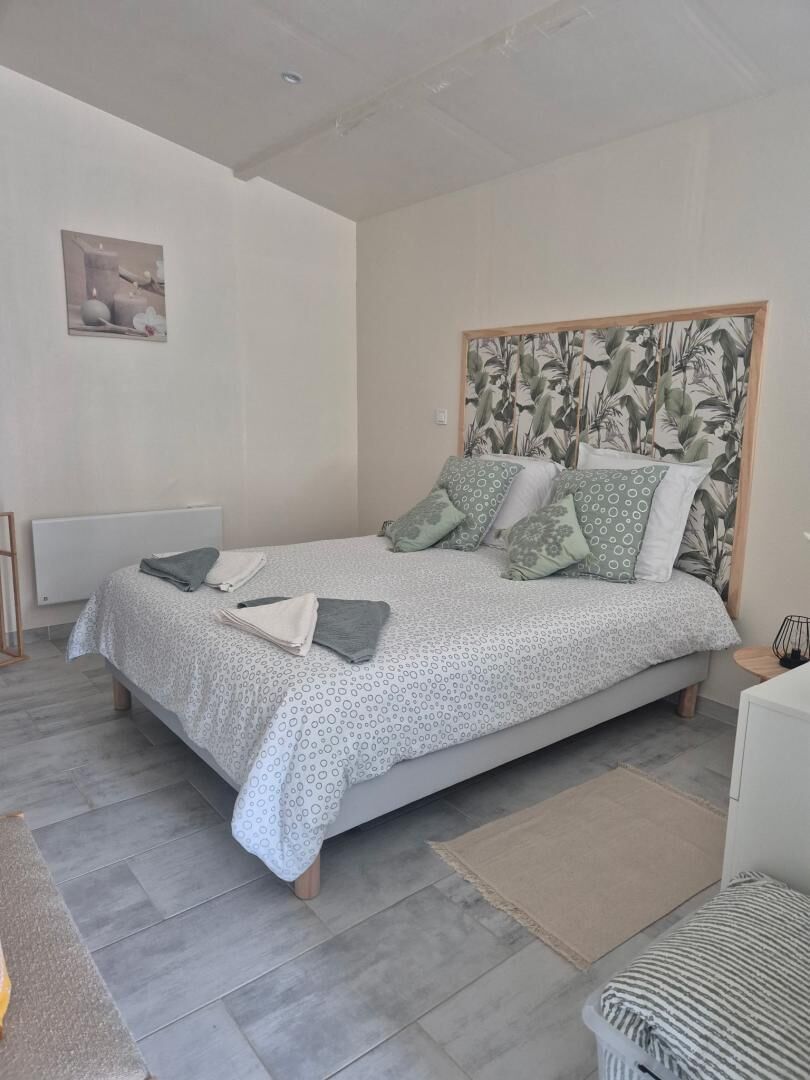 A bedroom with a bed, a headboard with a leaf pattern, a radiator, and a small table with a lamp.