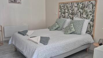 A bedroom with a bed, a headboard with a leaf pattern, a radiator, and a small table with a lamp.