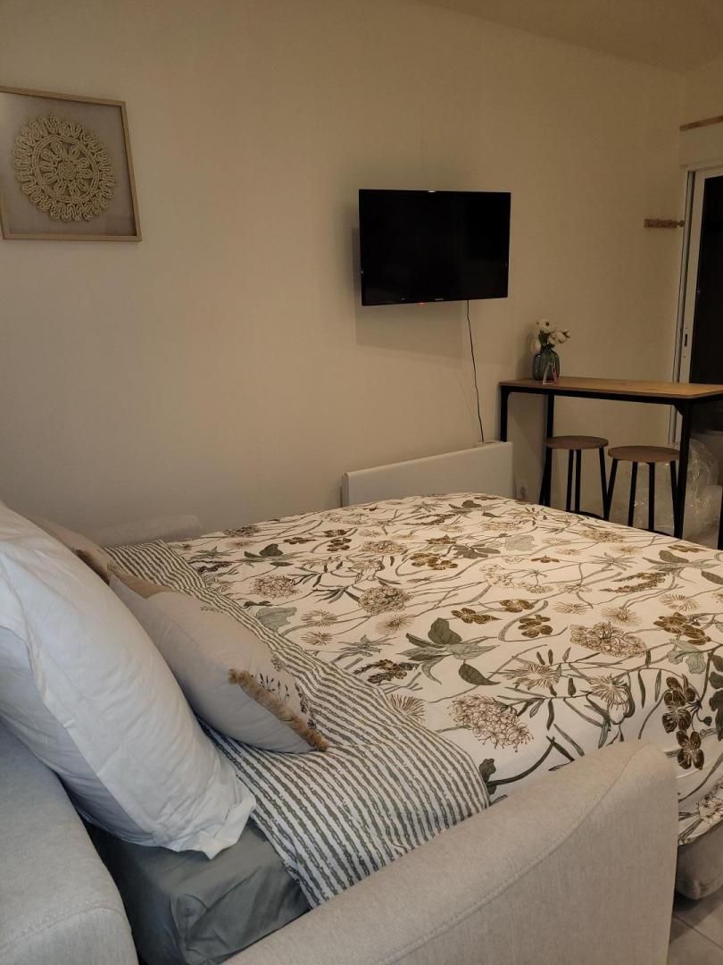 A bedroom with a bed, a TV mounted on the wall, a small table with a vase, and a chair.