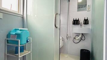 Un baño moderno con cabina de ducha de vidrio, un lavabo blanco y un estante con artículos de aseo.