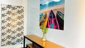 Una habitación con un banco de madera, un cuadro colgado en la pared que muestra kayaks en una playa y un papel tapiz estampado.