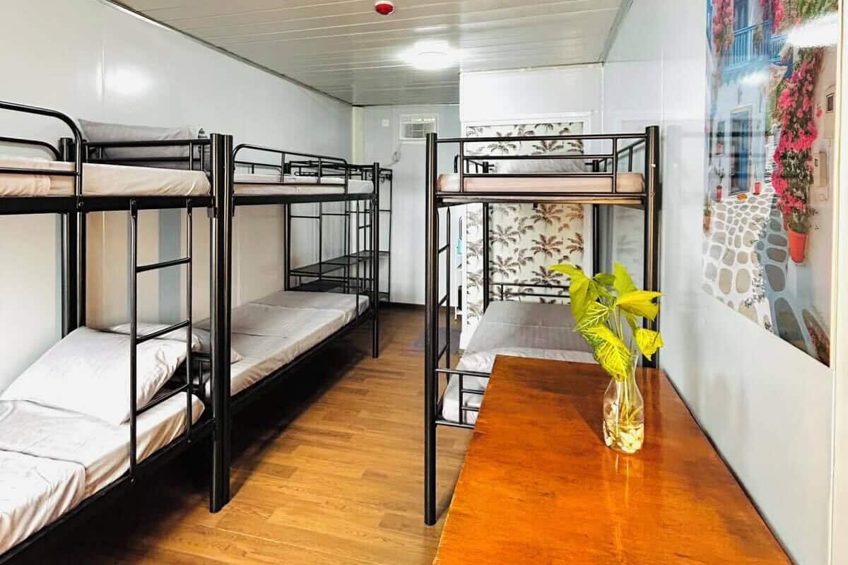 Een studentenkamer met stapelbedden, een houten tafel en een wand met een bloemenmural.