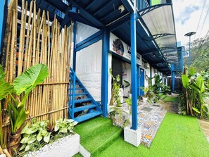 A building with a blue exterior and a covered entrance. There is a bamboo fence and various plants around. - Tandikan Suites El Nido (El Nido)