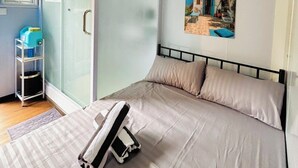 Un dormitorio con cama, una puerta corrediza, un ventanal, un estante con objetos y un cuadro en la pared.