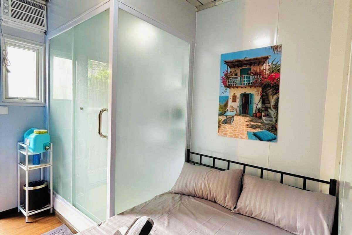 Een slaapkamer met een bed, een schuifdeur, een raam, een plank met spullen en een schilderij aan de muur.