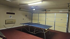 Une table de ping-pong dans une pièce dotée d’une porte de garage, d’un radiateur fixé au mur et d’un luminaire au plafond.