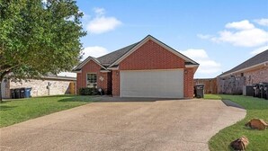 Une maison de plain-pied en briques, avec un garage, une pelouse bien entretenue et un ciel dégagé.