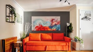 Ein modernes Wohnzimmer mit einem roten Sofa, einem Holztisch und einem großen abstrakten Gemälde an der Wand.