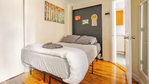 Ein Schlafzimmer mit Bett, Holzboden, einer Tür und einer Wand mit Kunstwerken.