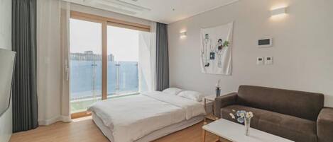 Una habitación de hotel moderna con una cama grande, un sofá, una mesa de centro y vistas a la ciudad.