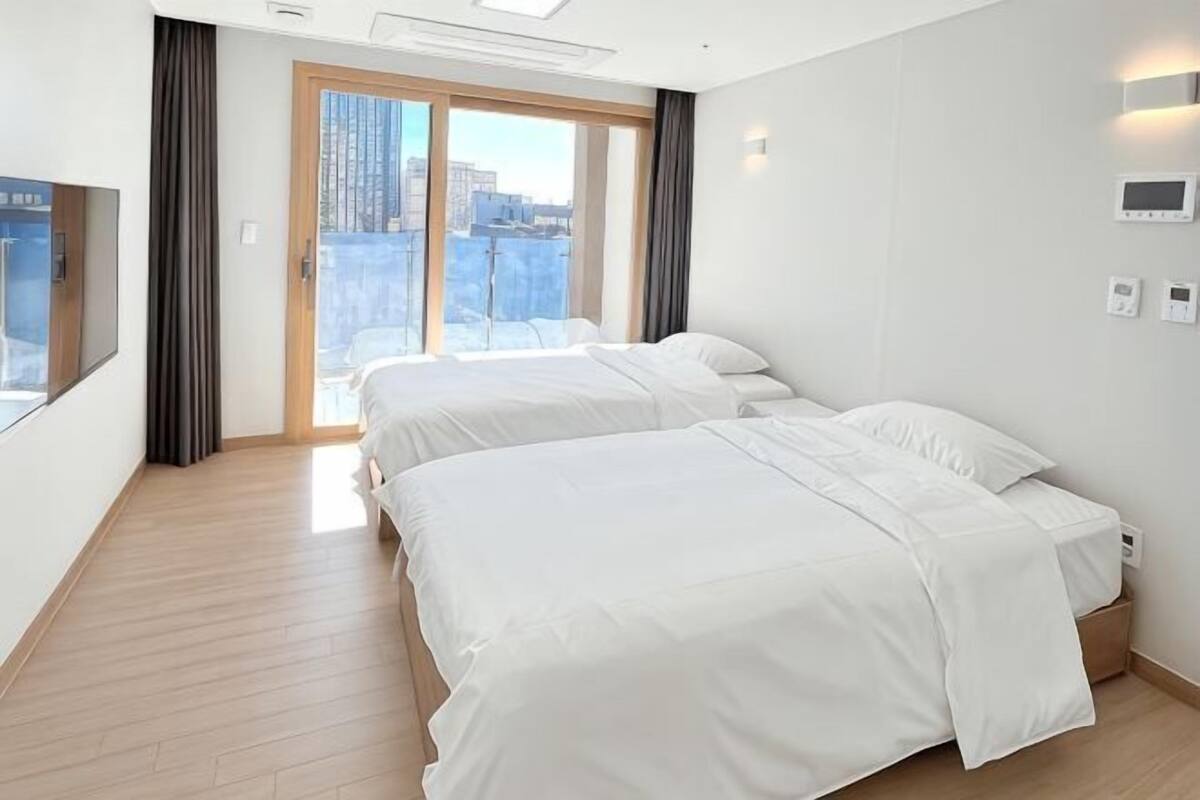 Une chambre d’hôtel avec deux lits, une grande fenêtre avec des rideaux, une vue sur la ville et un thermostat numérique.