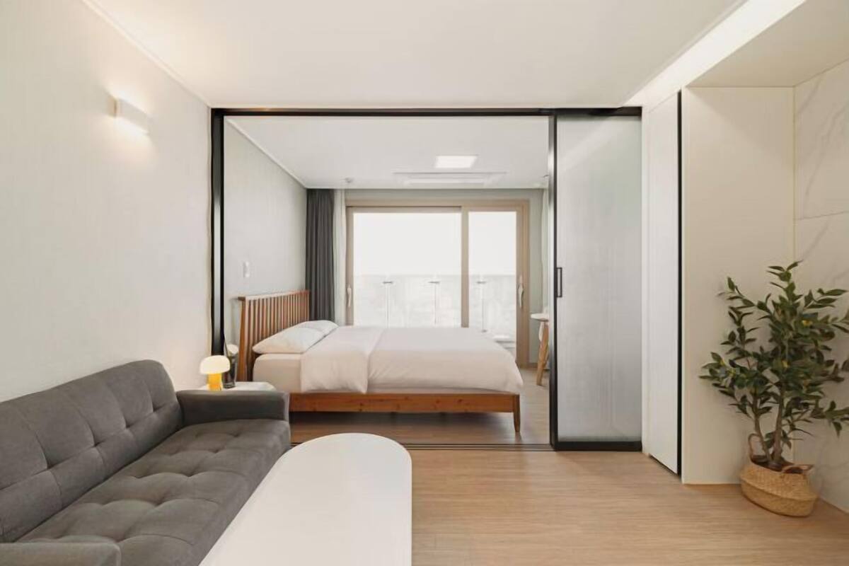 Une chambre moderne avec un lit, un canapé, une plante en pot et une vue à travers une porte vitrée.