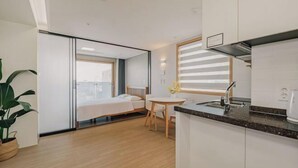 Une chambre d’hôtel moderne comprenant un lit, une petite table à manger, un coin cuisine et une grande fenêtre.