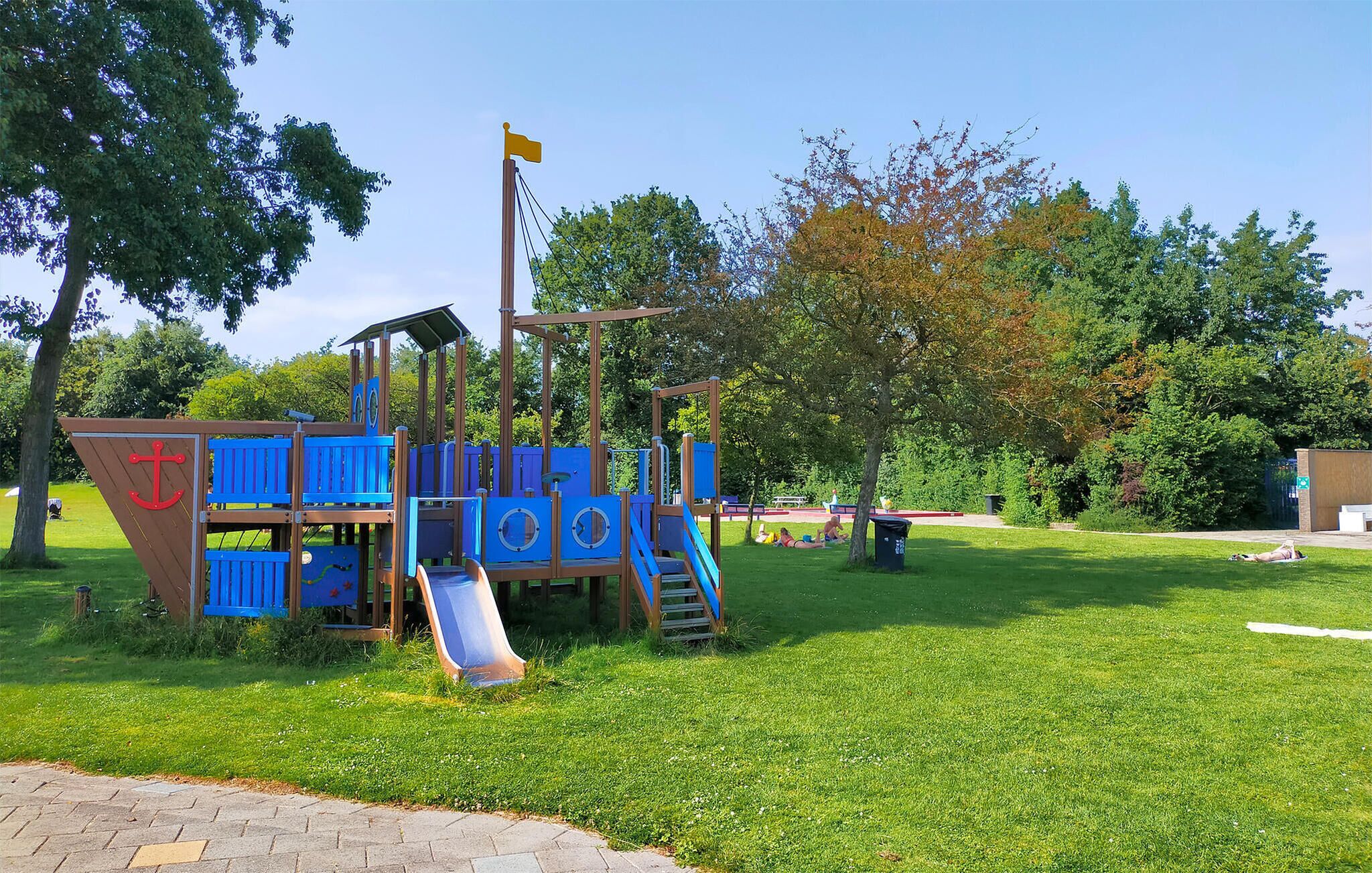 Ein Spielplatz mit Rutsche und Klettergerüsten, umgeben von Gras und Bäumen.