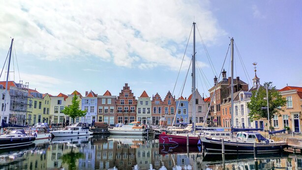 Een gracht met afgemeerde boten, omgeven door kleurrijke historische gebouwen.