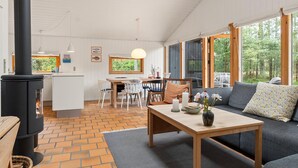 Ein gemütliches Blockhaus-Interieur mit Kamin, Essbereich und einer Sitzecke mit Blick auf den Wald.