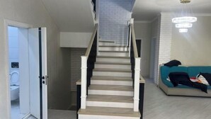 A staircase leading to a second floor, a living room with a sofa and a chandelier, and a bathroom with a toilet and sink. - HOMESTAY (Almaty)
