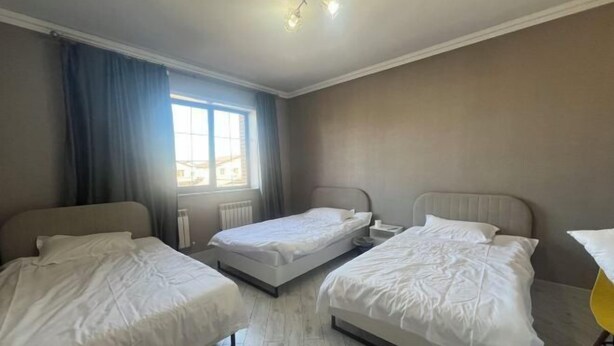 A room with three beds, a window with curtains, a radiator, and a ceiling light fixture. - HOMESTAY (Almaty)