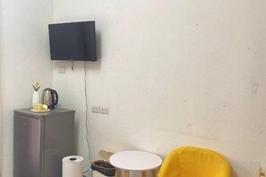 A room with a flat-screen TV mounted on the wall, a small table with a kettle and a vase, and a yellow chair. - Durian Family Hotel (Bangkok)