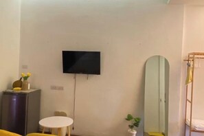 A room with a flat-screen TV mounted on the wall, a round table, a mirror, and a bunk bed. - Durian Family Hotel (Bangkok)