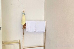 A room with a wooden drying rack holding white towels and a yellow cloth. - Durian Family Hotel (Bangkok)