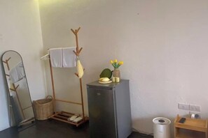 A compact room with a mirror, a coat rack, a small refrigerator, and a trash bin. - Durian Family Hotel (Bangkok)