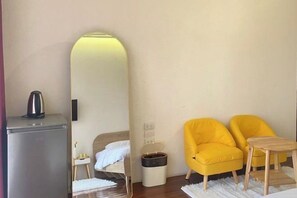 A room with a bed, a mirror, a small table, and two yellow chairs. - Durian Family Hotel (Bangkok)