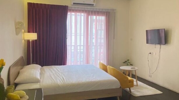 Ein Hotelzimmer mit einem Bett, einem an der Wand befestigten Fernseher, einem kleinen runden Tisch und einem Fenster mit Vorhängen.