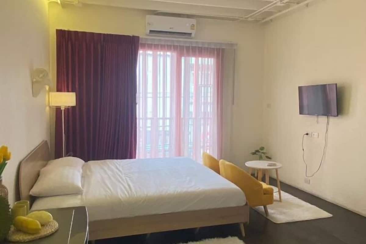 A hotel room with a bed, a TV mounted on the wall, a small round table, and a window with curtains.