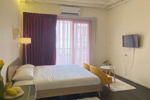 A hotel room with a bed, a TV mounted on the wall, a small round table, and a window with curtains. - Durian Family Hotel (Bangkok)