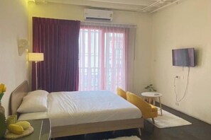 A hotel room with a bed, a television mounted on the wall, a small round table, and a window with curtains.