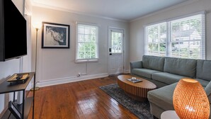 A living room with a flat-screen TV, a sofa, a coffee table, and a large window with blinds. - Heart of Midtown - Newly Renovated - Atlanta Home (Atlanta)